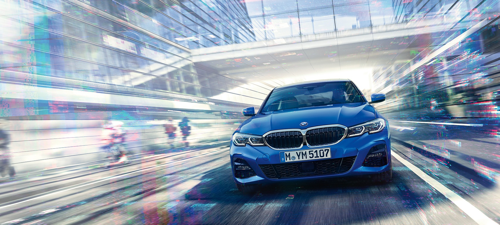 Front view of driving BMW 3 Series Sedan by day under glass building.