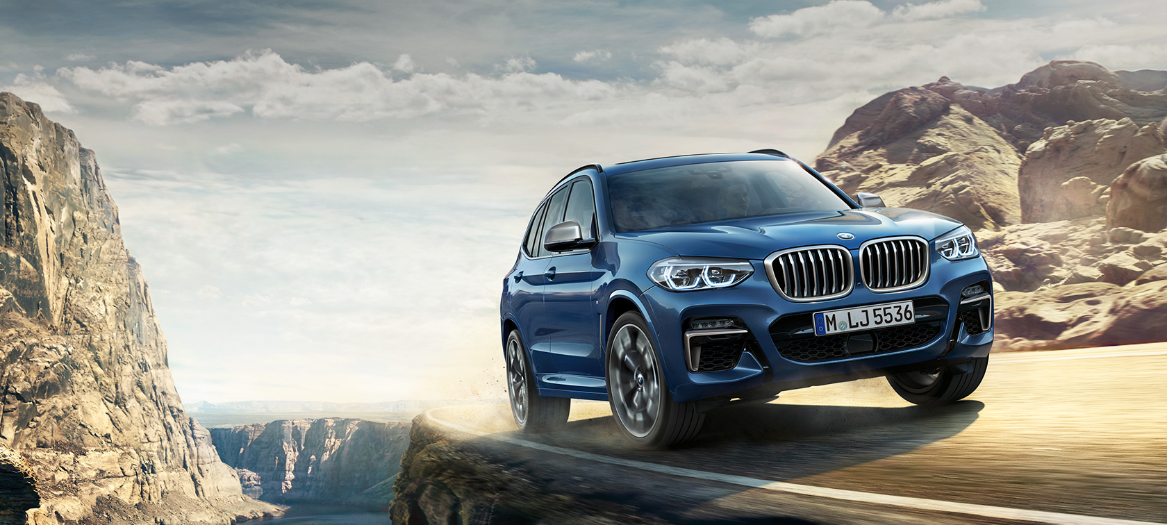 Front view of driving BMW 5 Series Sedan by day under glass building.